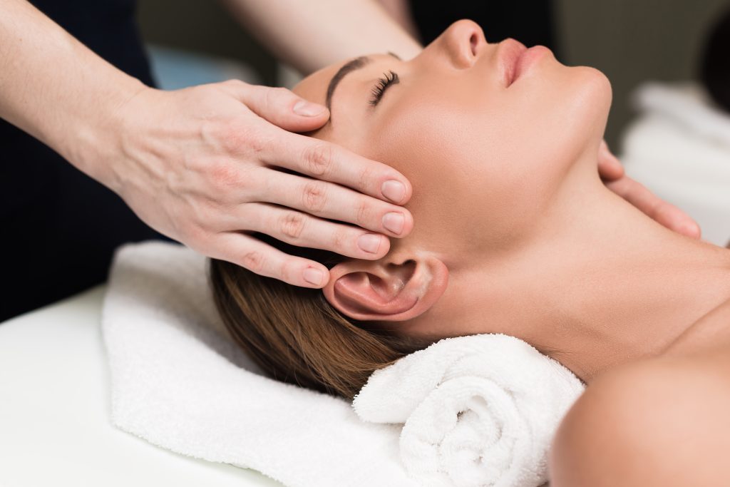 Close-up of a serene person receiving a head massage, hands gently placed on their temples. They lie on a towel, conveying relaxation and calm.