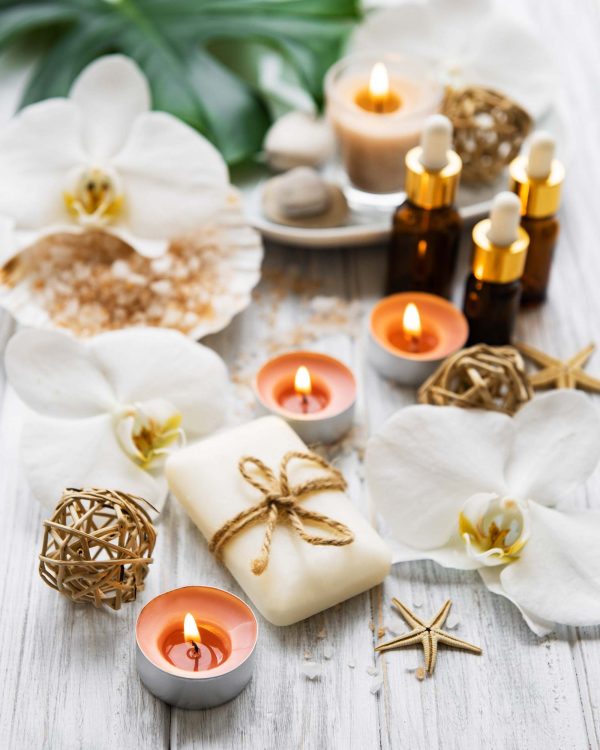 A serene spa scene with white orchids, lit candles, soap tied with twine, essential oil bottles, and decorative elements on a wooden surface.
